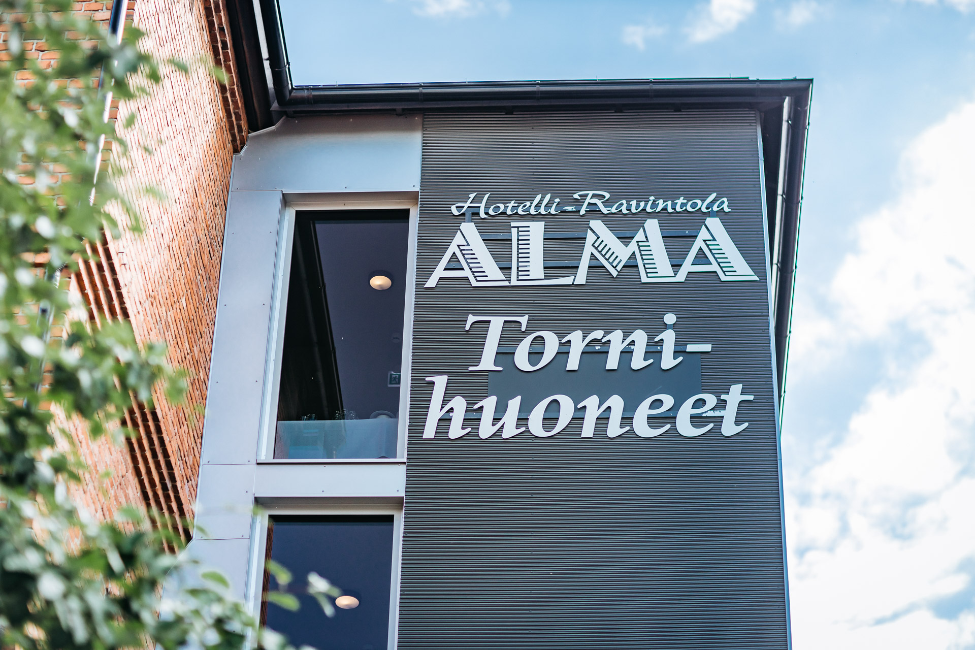 Hotelli Alma UKI Arkkitehdit Kuva tornihuoneiden logotekstistä julkisivussa.