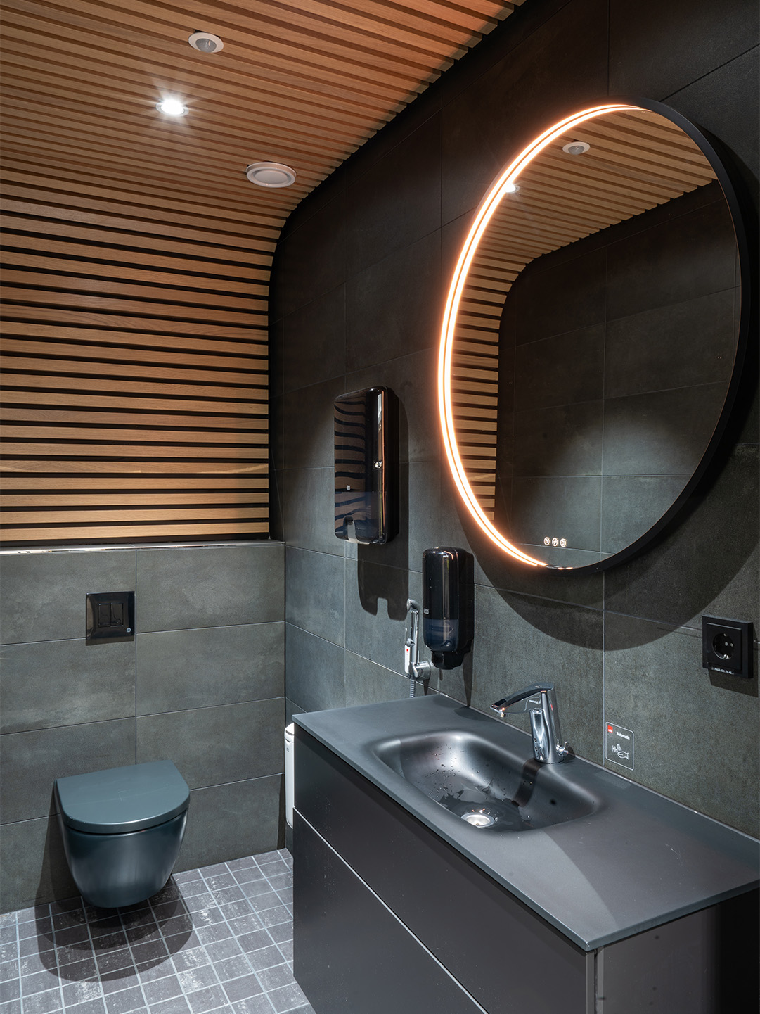 Kuva WC-tiloista jossa käytetty tummaa laattaa ja seinältä kattoon kääntyvää puurimoitusta.